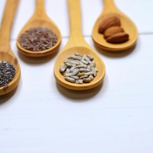 Home Close-up of various nuts and seeds in wooden spoons on a white background, showcasing healthy food options.